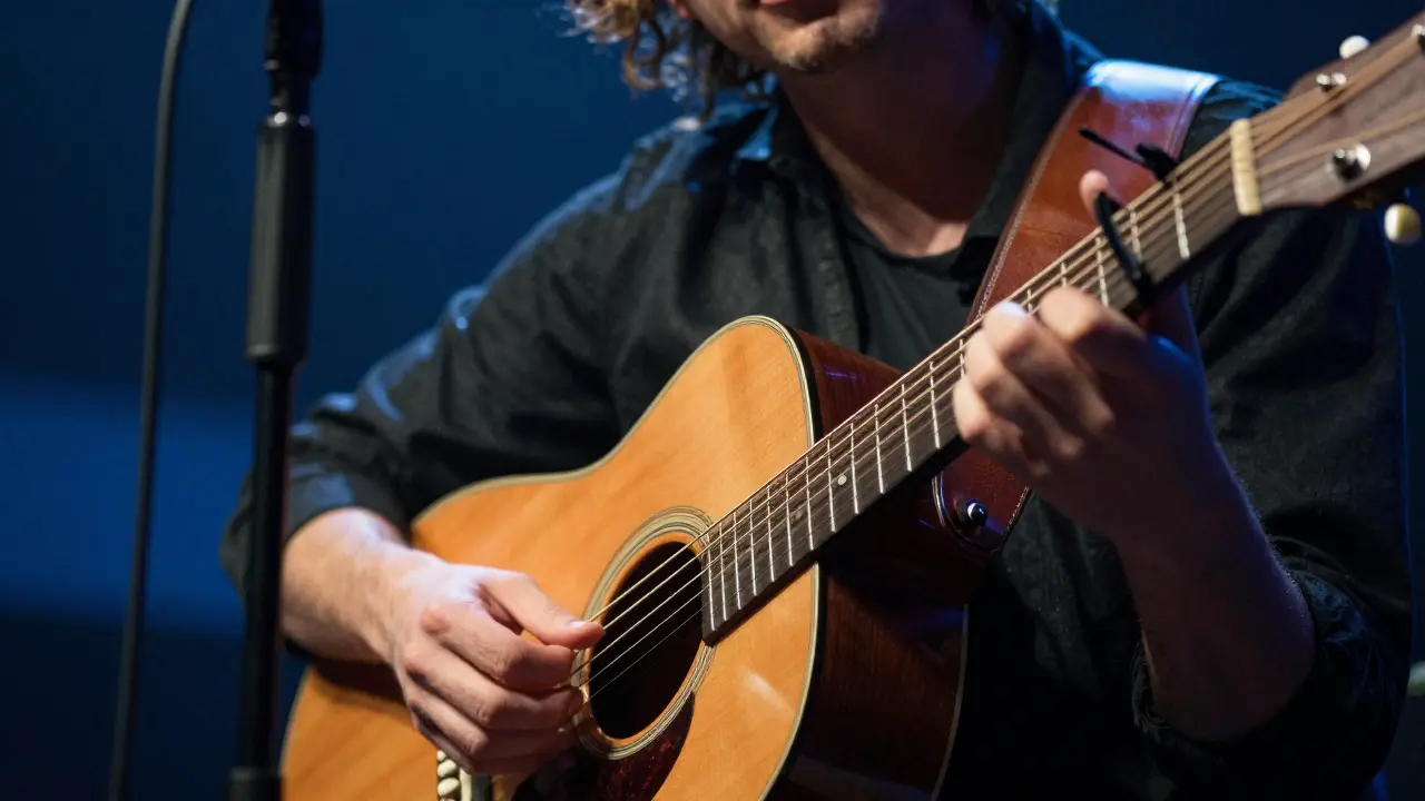 Close-up of hands playing an acoustic guitar with dramatic stage lighting